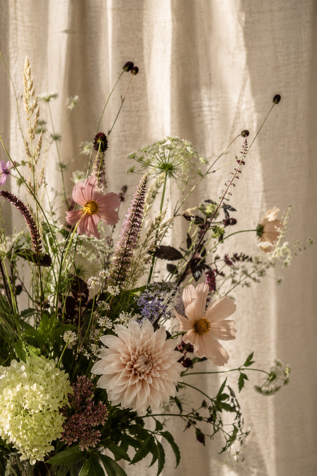 Blumenarrangement in warmem Licht vor einem hellen Vorhang